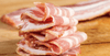 Strips of bacon piled up on a cutting board