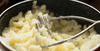 A pot of mashed potatoes with a potato masher